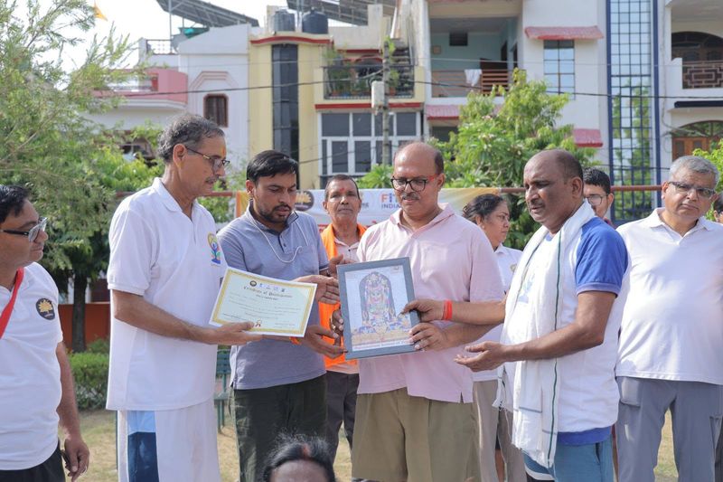 A certificate and a framed picture being handed to a participant outdoors, with other attendees looking on