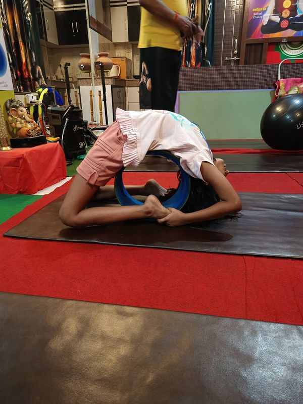 A child arching backwards over a blue yoga wheel on a mat, hands reaching the feet