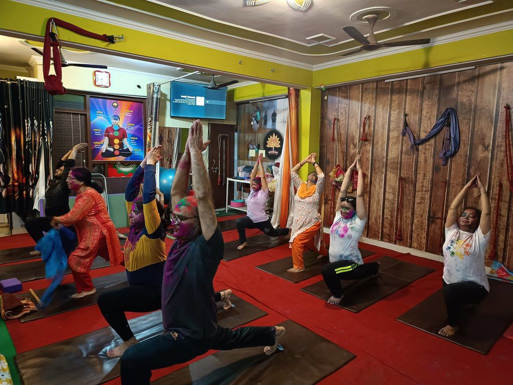 Students with Holi colours on their faces and clothes holding a lunge with arms raised, in the studio