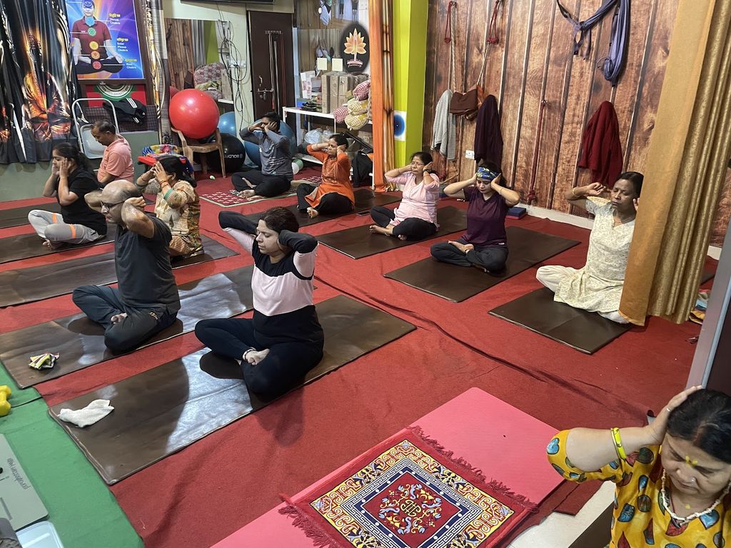 A morning group class at Purushottam School of Yoga: about a dozen students seated cross-legged on mats in the wood-panelled studio, hands resting behind their heads