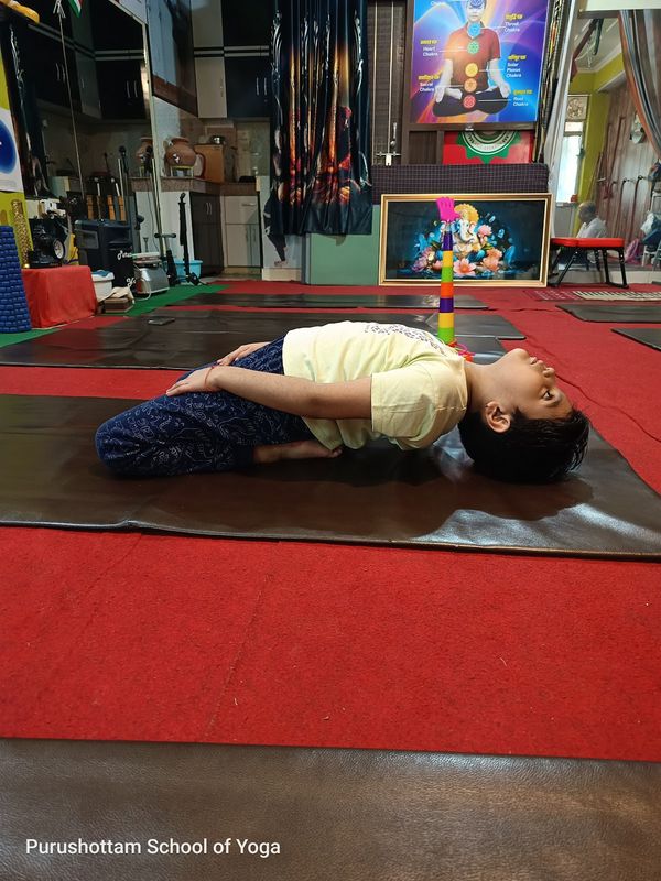 A child lying in a supported backbend on a yoga mat inside the studio
